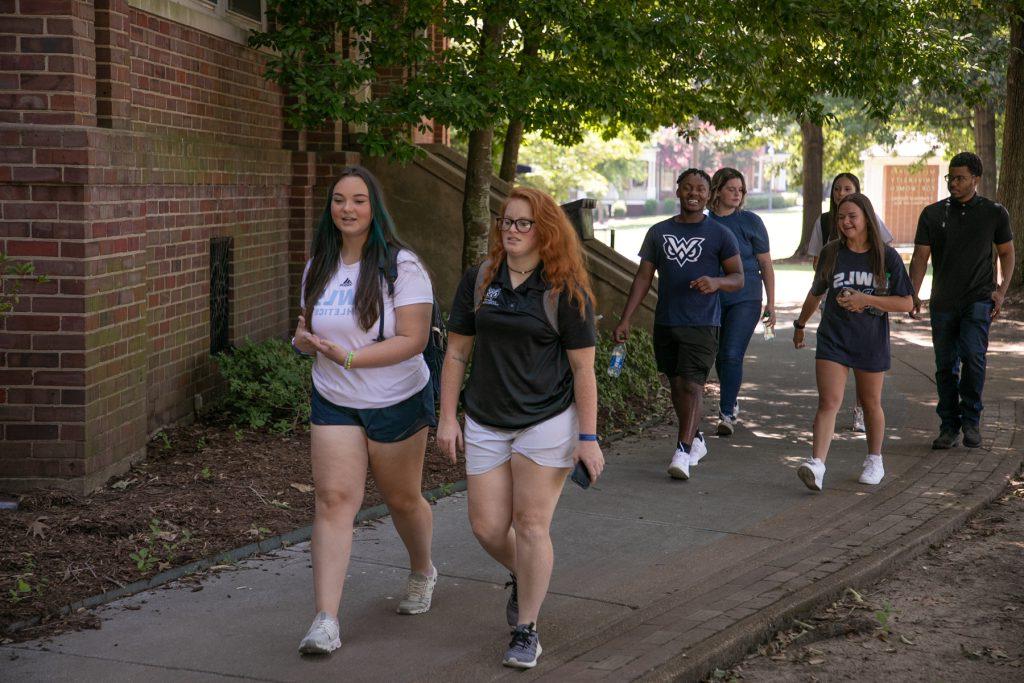 A group of students, 5 women and 3 men, walk past historic Callaway Hall