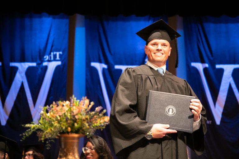 毕业典礼上，一名头戴帽子、身穿长袍的男子在台上拿着学位证书